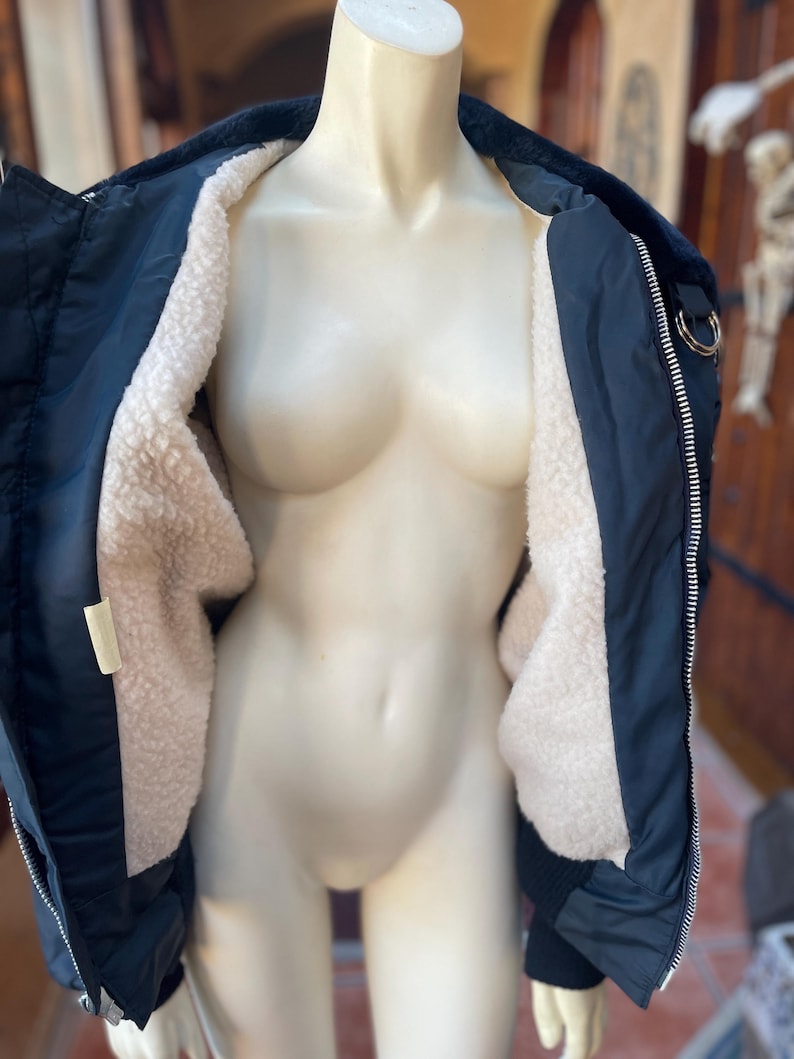 May include: A navy blue bomber jacket with a white sherpa lining. The jacket has a zipper closure and two pockets on the front.