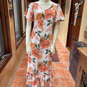 May include: A white maxi dress with a floral print in shades of orange and green. The dress has a ruffled hem and short sleeves.