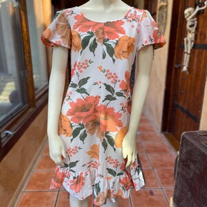May include: A white dress with a floral print in shades of orange and green. The dress has short sleeves and a ruffled hem.