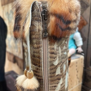 May include: Close-up of a brown and tan leather boot with a fur trim. The boot features a zipper with the text "el dante" and a decorative tassel. The boot has a snakeskin pattern with cut-out designs.