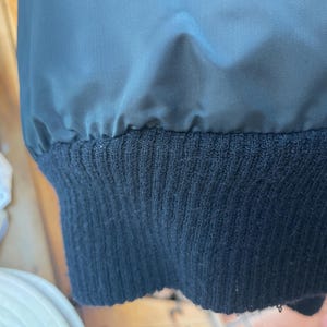 May include: Close-up of the black ribbed knit cuff of a jacket. The cuff is made of a soft, comfortable material.