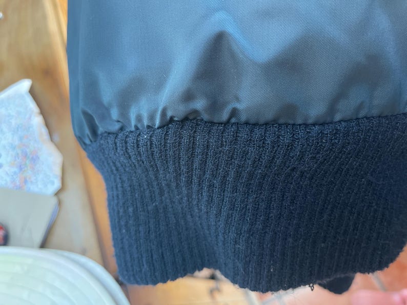 May include: Close-up of the black ribbed knit cuff of a jacket. The cuff is made of a soft, comfortable material.