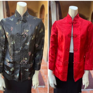 May include: Two silk jackets on mannequins. One is black with a floral pattern and frog closures. The other is red with a subtle embossed design and similar closures. Both have mandarin collars and pockets.