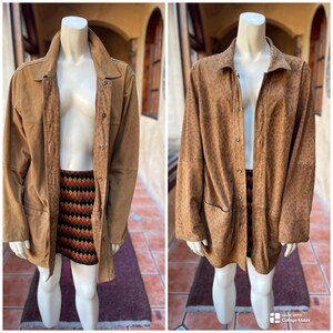 May include: Two tan suede jackets displayed on mannequins. One is a solid color, the other has a leopard print. Both have button closures and pockets. The mannequins are also wearing a patterned skirt.