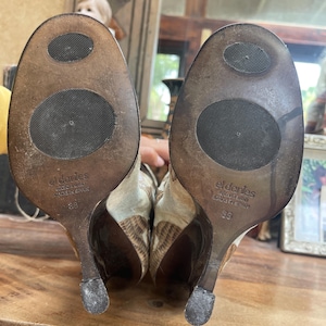 May include: A pair of high-heeled shoes with a textured, patterned design in shades of brown and beige. The soles are visible, showing the brand name "eldanies" and size 38. The heels are dark brown.