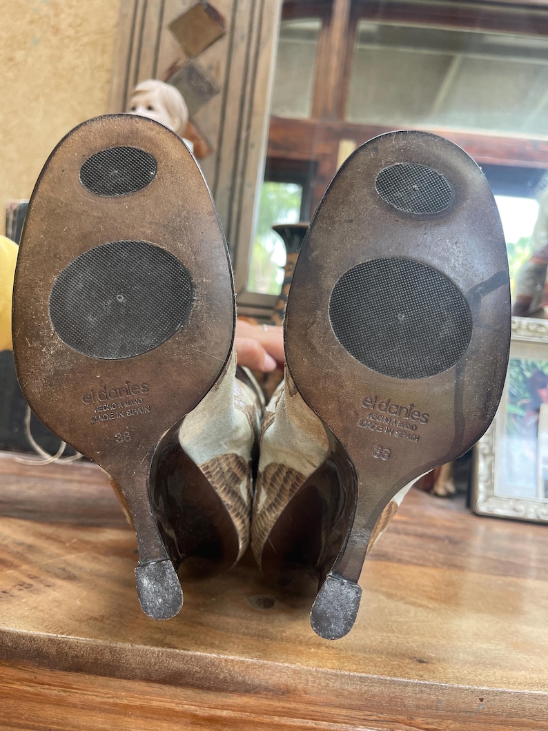 May include: A pair of high-heeled shoes with a textured, patterned design in shades of brown and beige. The soles are visible, showing the brand name "eldanies" and size 38. The heels are dark brown.