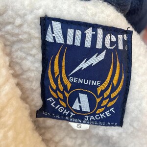 May include: A blue and yellow patch with the text "Antler Genuine Flight Jacket" and a lightning bolt graphic. The patch has a white border and the text "Reg. T.M. - M. Rubin & Sons, Inc. N.Y.C." is printed below the main text.