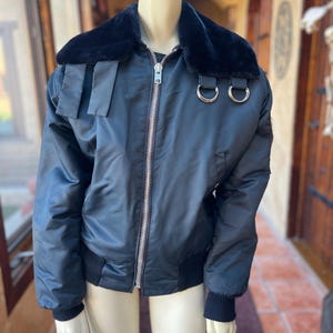 May include: A black bomber jacket with a faux fur collar and silver zipper. The jacket has two silver rings on the collar and a black ribbed knit at the cuffs and hem.