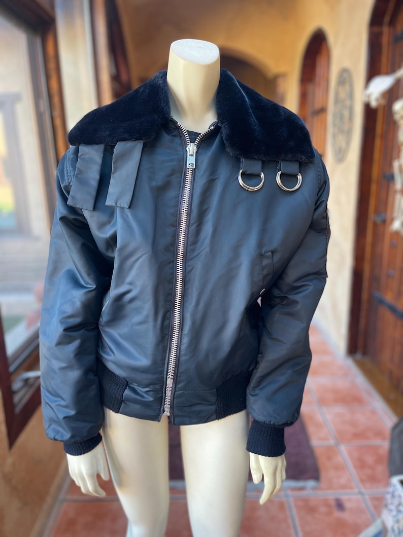 May include: A black bomber jacket with a faux fur collar and silver zipper. The jacket has two silver rings on the collar and a black ribbed knit at the cuffs and hem.