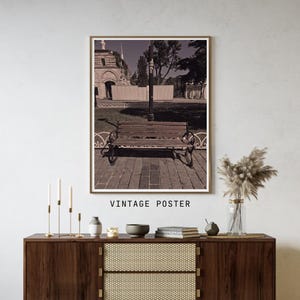 May include: A framed wall poster featuring a sepia-toned photograph of a wooden park bench situated on a paved path in front of a stone building and trees. The text VINTAGE POSTER is printed in black capital letters below the framed image.
