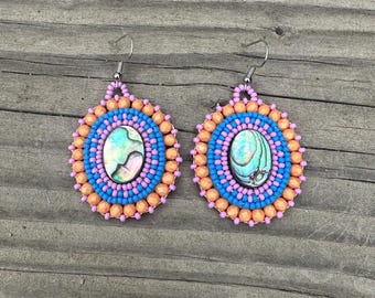 May include: A pair of circular dangle earrings featuring a central oval abalone shell cabochon surrounded by concentric rings of bright blue, light pink, and peach-colored beads, finished with silver-toned metal earring hooks for pierced ears.