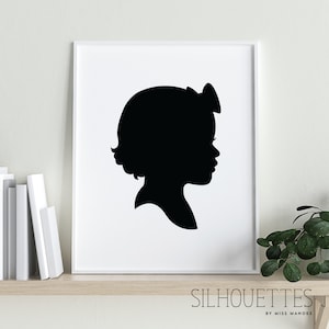 May include: Black and white silhouette of a child with a bow in their hair, printed on a white background and framed in a white frame.