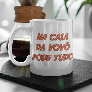 May include: White ceramic mug with a black handle. The mug has orange text that reads "NA CASA DA VOVÓ PODE TUDO".