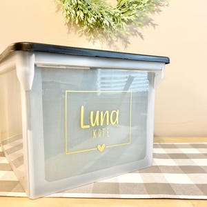May include: A white plastic storage box with a black lid. The box has a gold label with the name "Luna Kate" and a small heart.