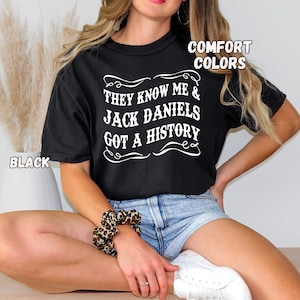 Könnte beinhalten: Ein schwarzes T-Shirt mit weißem Text, der "They know me & Jack Daniels got a history" lautet. Das Shirt wird von einer Person getragen, die eine Jeans-Shorts trägt.