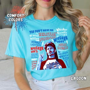 May include: A turquoise t-shirt with a graphic featuring a man with a mullet and text. The text includes phrases like "You don't have no..." and "Hoosker Doos." The shirt also has the words "Comfort Colors" and "Lagoon."