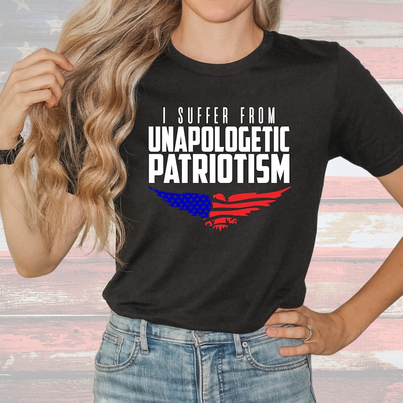 Op de afbeelding: Zwart T-shirt met een witte adelaar afbeelding en de tekst "I suffer from unapologetic patriotism". De adelaar heeft rood-wit-blauwe strepen op zijn vleugels.