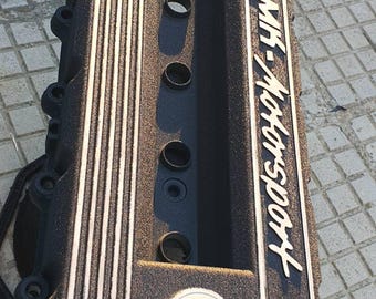 Può includere: Coperchio valvole motore nero con strisce verticali bianche e la scritta "MK-Motorsport". Il coperchio presenta diverse aperture circolari e una superficie strutturata. Ricambio auto.
