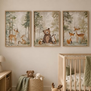 May include: Three rectangular wall art prints in light wood frames featuring watercolor forest scenes with woodland animals including a deer, rabbit, hedgehog, bear, badger, and fox, displayed above a wooden crib and a storage unit.