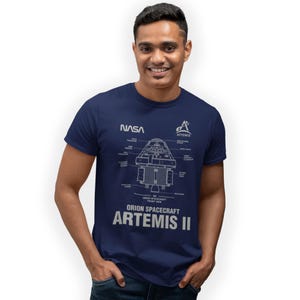 May include: A navy blue t-shirt displaying a diagram of the Orion Spacecraft Artemis II, with NASA and Artemis logos. The design includes technical labels and a front view illustration. The shirt has a crew neck.