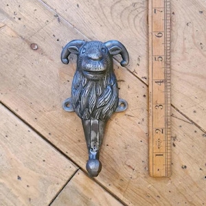 May include: A cast iron coat hook shaped like a ram's head with a textured, furry finish. The hook is painted in a dark grey colour and has a long, pointed tail.