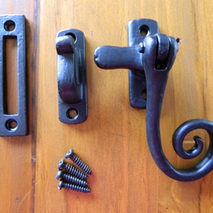 May include: Black metal window latch with a decorative scroll design. The latch includes a strike plate and mounting screws.