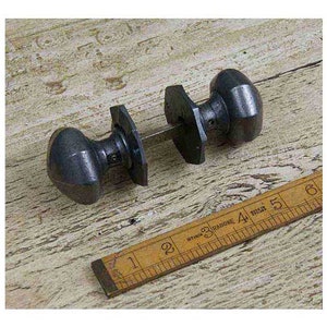 May include: A pair of black cast iron door knobs with a square backplate. The knobs are round and have a slightly domed shape.