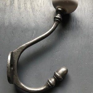 May include: A cast iron hook with a white ceramic knob and an acorn-shaped finial. The hook is designed for hanging items on a wall.