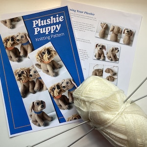 May include: A knitting pattern for a plushie puppy, with photos of the finished product. The pattern includes instructions for knitting the body, head, ears, and tail. A ball of white yarn and knitting needles are also included.