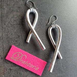 Könnte beinhalten: Ein Paar silberne Ohrringe aus Metall mit einem gedrehten Design. Die Ohrringe sind handgefertigt und haben einen einzigartigen, modernen Look.