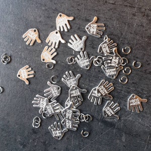 Könnte beinhalten: Eine Sammlung silberner handförmiger Anhänger mit der Gravur "Hand Made". Die Anhänger haben Sprungringe.
