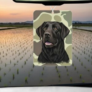 Pode incluir: Ambientador retangular com um Labrador Retriever preto sobre um fundo de camuflagem. O c&atilde;o &eacute; retratado com um estilo detalhado, com foco no seu rosto. Pendurado por um fio, presumivelmente para um carro.