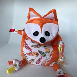 May include: Orange and white plush fox toy with a feather pattern. The toy has a pacifier attached and is designed for babies.