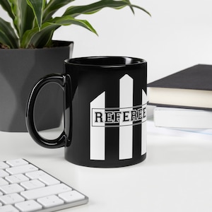 May include: Black ceramic mug with a white and black striped design and the word "REFEREE" in white letters.
