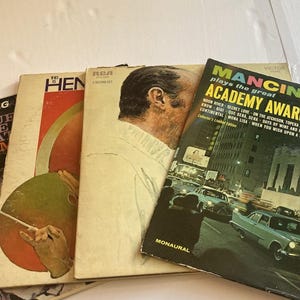 May include: A collection of vintage vinyl record albums. Album covers feature portraits, abstract designs, and cityscapes. Titles include "The Blue and the Beat," "Mancini Plays the Great Academy Award Songs," and "HEN."