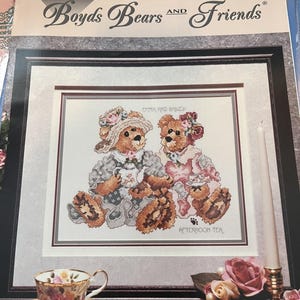 May include: A cross stitch pattern booklet titled Boyds Bears and Friends Emma & Bailey Afternoon Tea. The cover features an illustration of two brown teddy bears wearing hats and outfits, holding tea sets, with the text Emma and Bailey Afternoon Tea.