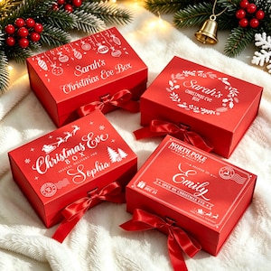 May include: Four rectangular red gift boxes with lids and satin ribbon closures. Each box features white printed holiday designs and names including Sarah's Christmas Eve Box, Sarah's Christmas Eve Box, Christmas Eve Box for Sophia, and North Pole Express Delivery for Emily.