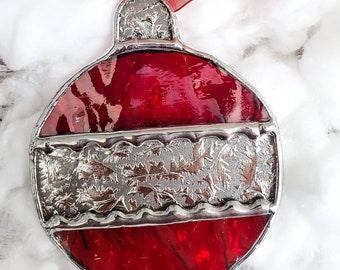 May include: A red glass Christmas ornament with a silver, textured band around the middle. The ornament is shaped like a traditional Christmas ball.