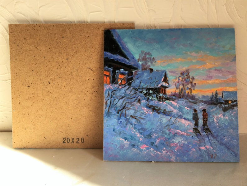 May include: A painting of a snowy winter scene with two houses, one with lit windows, and two figures walking in the snow. The sky is a vibrant blue with pink and orange hues. The painting is 20 inches by 20 inches.