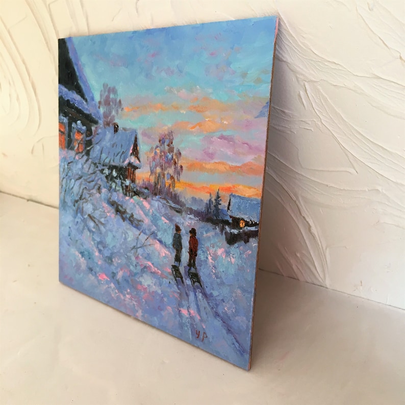 May include: A painting of a snowy winter scene with two figures walking in the foreground. The sky is a vibrant blue with pink and orange clouds. There are two houses in the background, one with a lit window. The painting is done in a realistic style with visible brushstrokes.