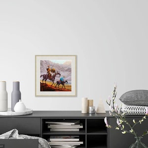 May include: A framed painting of two figures on horseback riding through a desert landscape. The figures are wearing traditional clothing and the horses are brown. The background is a muted brown and gray.