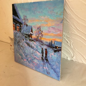May include: A painting of a snowy winter scene with two figures walking in the distance. The sky is a vibrant mix of pink, orange, and blue, with a few clouds. The houses in the background are covered in snow, and the trees are bare. The painting is done in a realistic style, with visible brushstrokes.