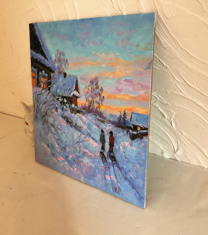 May include: A painting of a snowy winter scene with two figures walking in the distance. The sky is a vibrant mix of pink, orange, and blue, with a few clouds. The houses in the background are covered in snow, and the trees are bare. The painting is done in a realistic style, with visible brushstrokes.