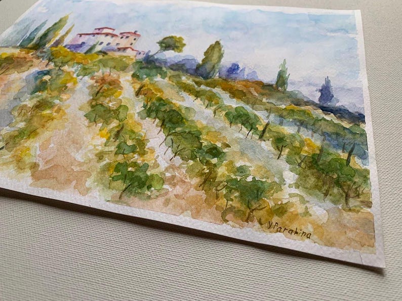 Op de afbeelding: Waterverfschilderij van een wijngaard met rijen groene wijnranken op een heuvel. Een gebouw met rode pannendaken is zichtbaar. De lucht is lichtblauw en de voorgrond is een mix van geel en bruin.