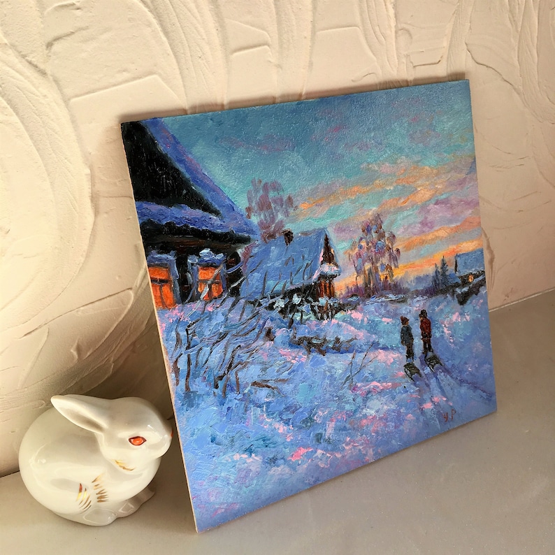 May include: A painting of a snowy winter scene with two small houses and two figures walking in the distance. The sky is a vibrant blue with pink and orange hues. The houses are covered in snow and the trees are bare.