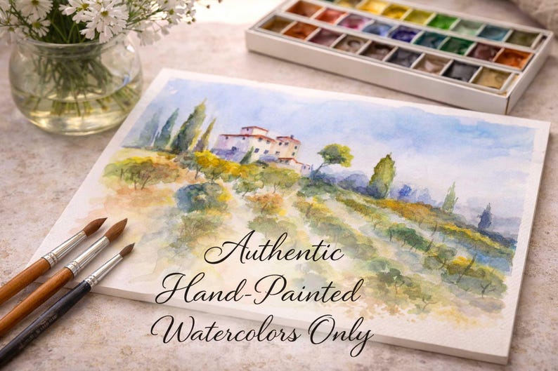 Op de afbeelding: Een aquarel van een Toscaans landschap met heuvels, bomen en een gebouw. De schildering staat op een wit canvas met de tekst "Authentic Hand-Painted Watercolors Only." Penselen en een aquarelpalet zijn ook zichtbaar.