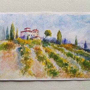 Op de afbeelding: Waterverfschilderij van een Toscaans landschap met een villa met een rood pannendak, omgeven door wijngaarden en hoge cipressen. Het kunstwerk gebruikt zachte blauwe, groene en gele tinten om de glooiende heuvels en de lucht weer te geven.