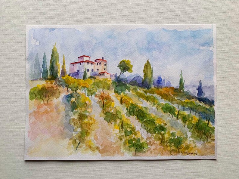 Op de afbeelding: Waterverfschilderij van een Toscaans landschap met een villa met een rood pannendak, omgeven door wijngaarden en hoge cipressen. Het kunstwerk gebruikt zachte blauwe, groene en gele tinten om de glooiende heuvels en de lucht weer te geven.