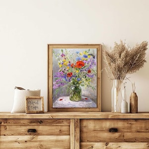 May include: A framed floral painting featuring a vibrant bouquet of wildflowers in a glass jar. The artwork showcases a mix of red, purple, yellow, and blue flowers, set against a soft, neutral background. The painting is displayed on a wooden dresser.