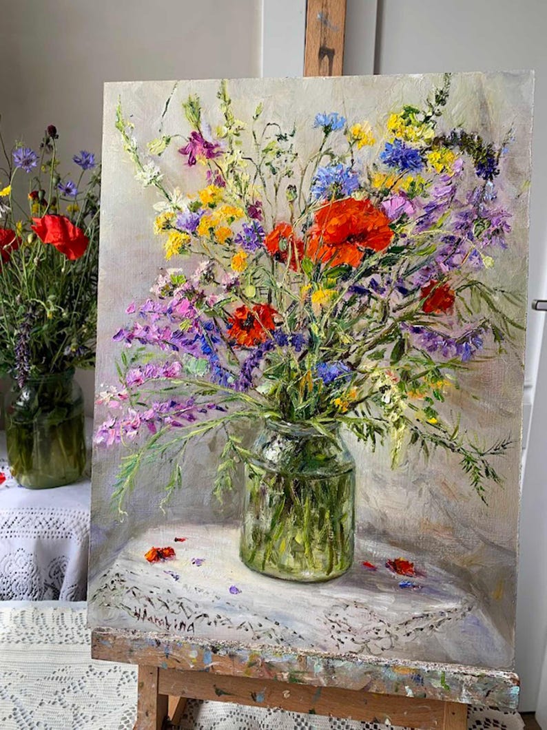May include: An oil painting of a vibrant bouquet of wildflowers in a clear glass jar. The flowers include red poppies, purple, yellow, and blue blossoms. The jar sits on a white lace tablecloth, with a second jar of flowers in the background.